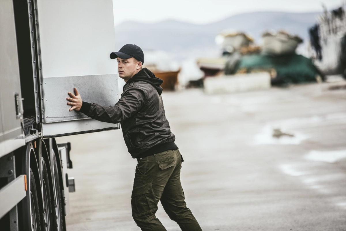 Samochód ciężarowy Volvo z 2 naczepami na których znajdują się kontenery. W tle widać magazyn kontenerów na wolnym powietrzu.