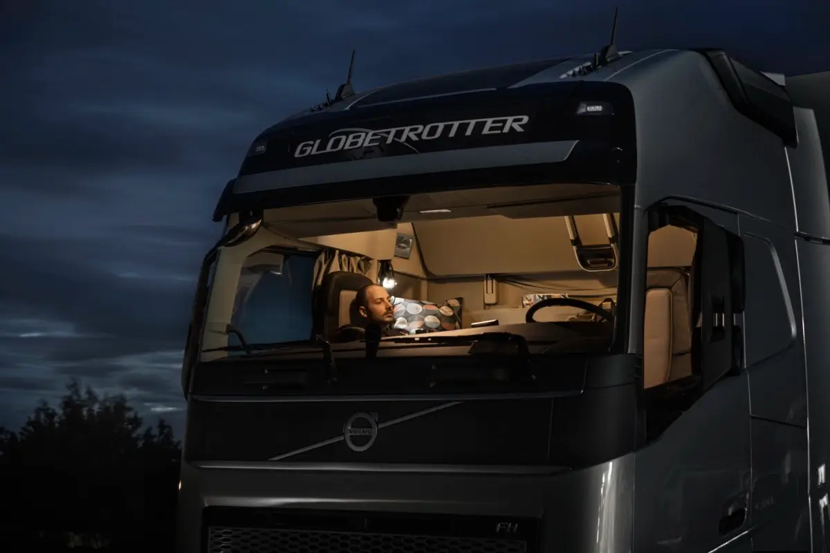 Pojazd ciężarowy Volvo przejeżdżający o zmierzchu zaśnieżoną drogą w tle widać światło miasta