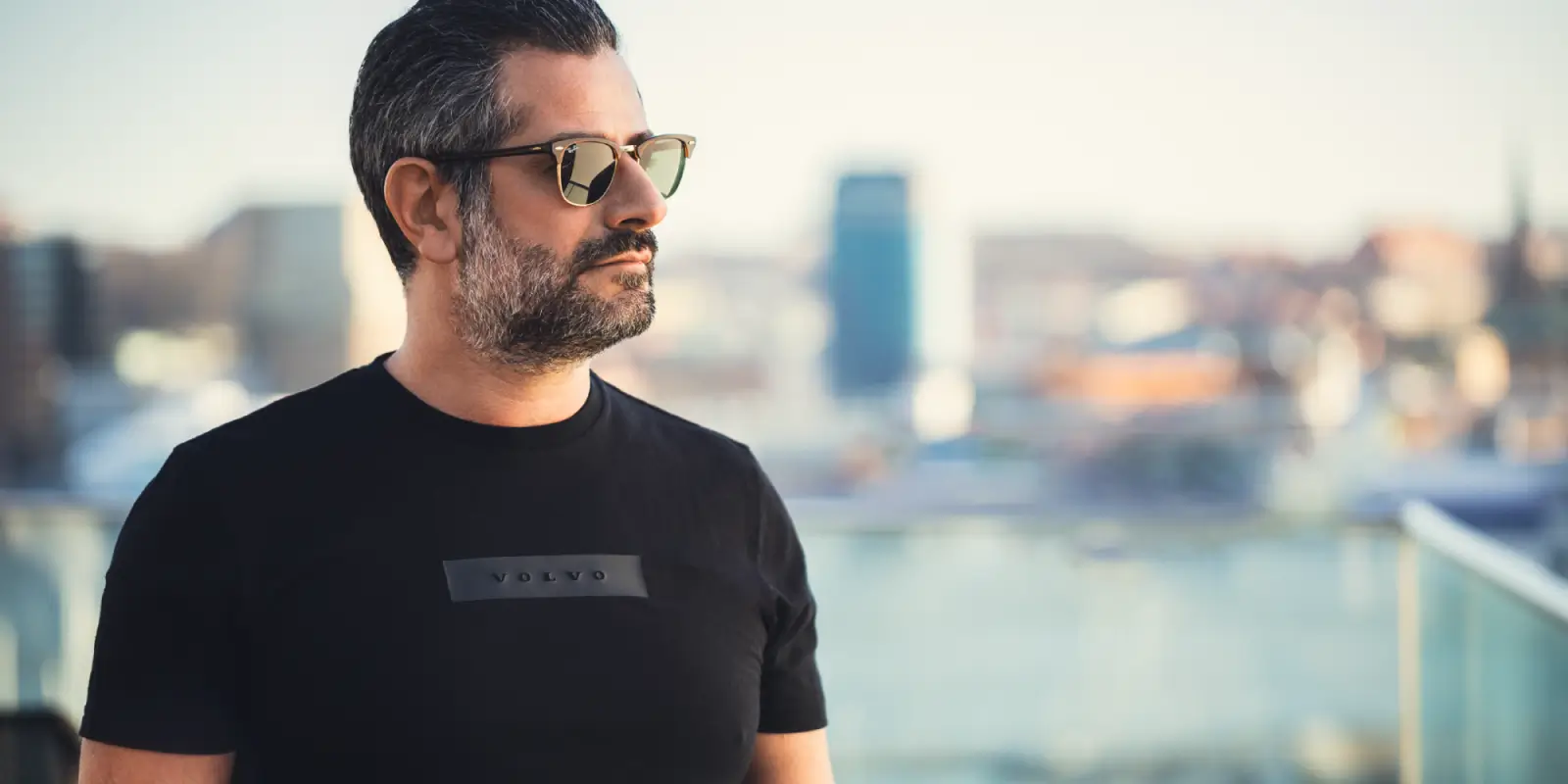 Mężczyzna w okularach w czarnej koszulce z logiem Volvo. Tło jest dość mocno rozmyte