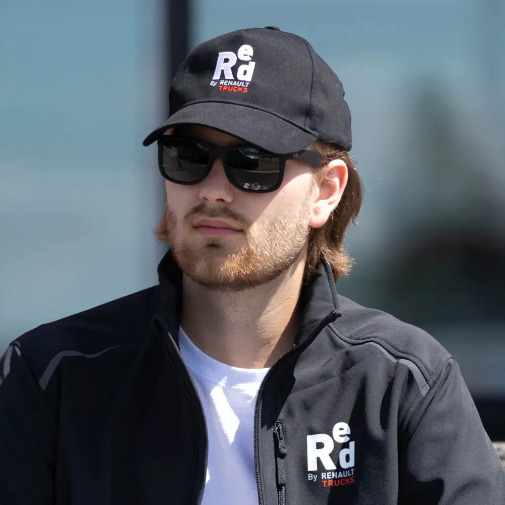 Mężczyzna ubrany w polar oraz czapkę z daszkiem koloru czarnego sygnowane logiem Renault Trucks, tło jest mocno rozmyte