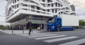 Mężczyzna przechodzi przez przejście dla pieszych w tle widać budynek oraz elektryczny samochód ciężarowy Renault