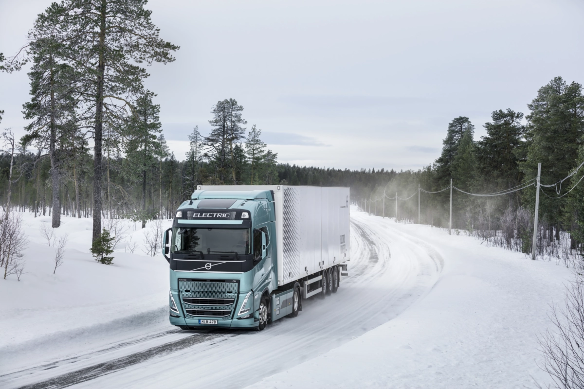 Pojazd ciężarowy Volvo przejeżdżający o zmierzchu zaśnieżoną drogą w tle widać światło miasta
